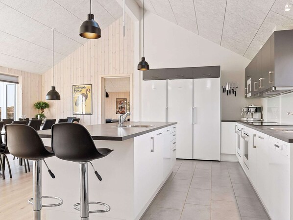 A modern kitchen with white cabinetry, stainless steel appliances, and a central island with bar stools. - Holiday Home in Kappeln (Kappeln)