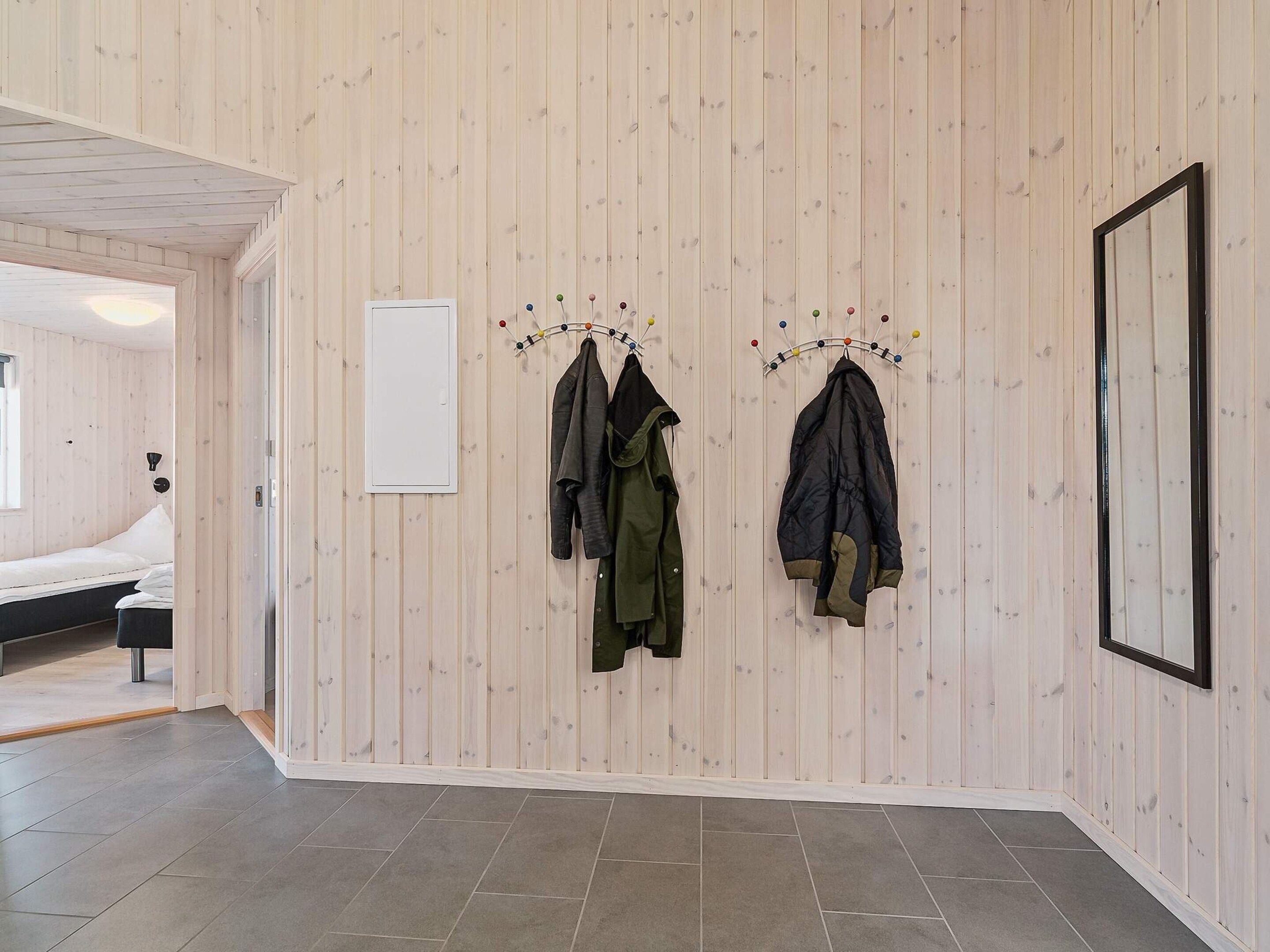 Una habitación con una cama, un perchero con chaquetas, un cuadro enmarcado y una pared de madera.