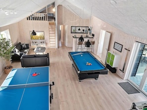 A modern living room with a pool table, a sofa, a dining area, and a staircase leading to an upper level.