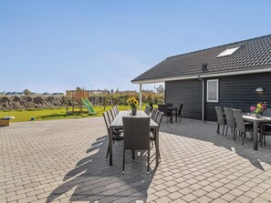 An outdoor patio with a table and chairs, a play area with a slide, and a building with a dark exterior.