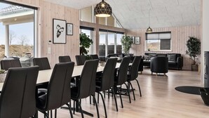 Ett modernt matområde med ett långt bord och stolar, stora fönster och utsikt över omgivningen.