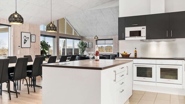 Ett modernt kök med vita skåp, en stor köksö och en matplats med stolar och bord.