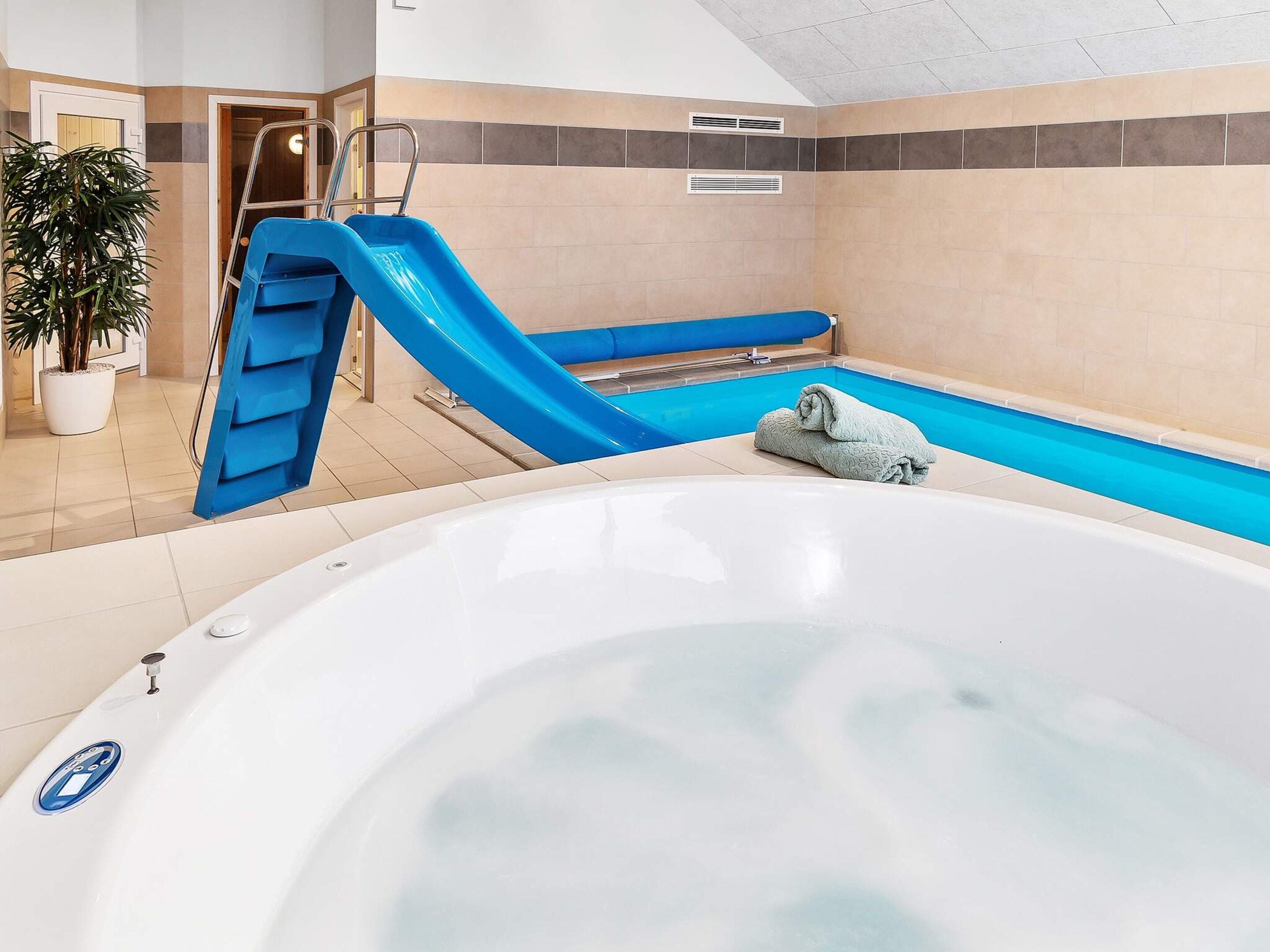 Un área de piscina con jacuzzi, un tobogán azul y una planta en maceta.