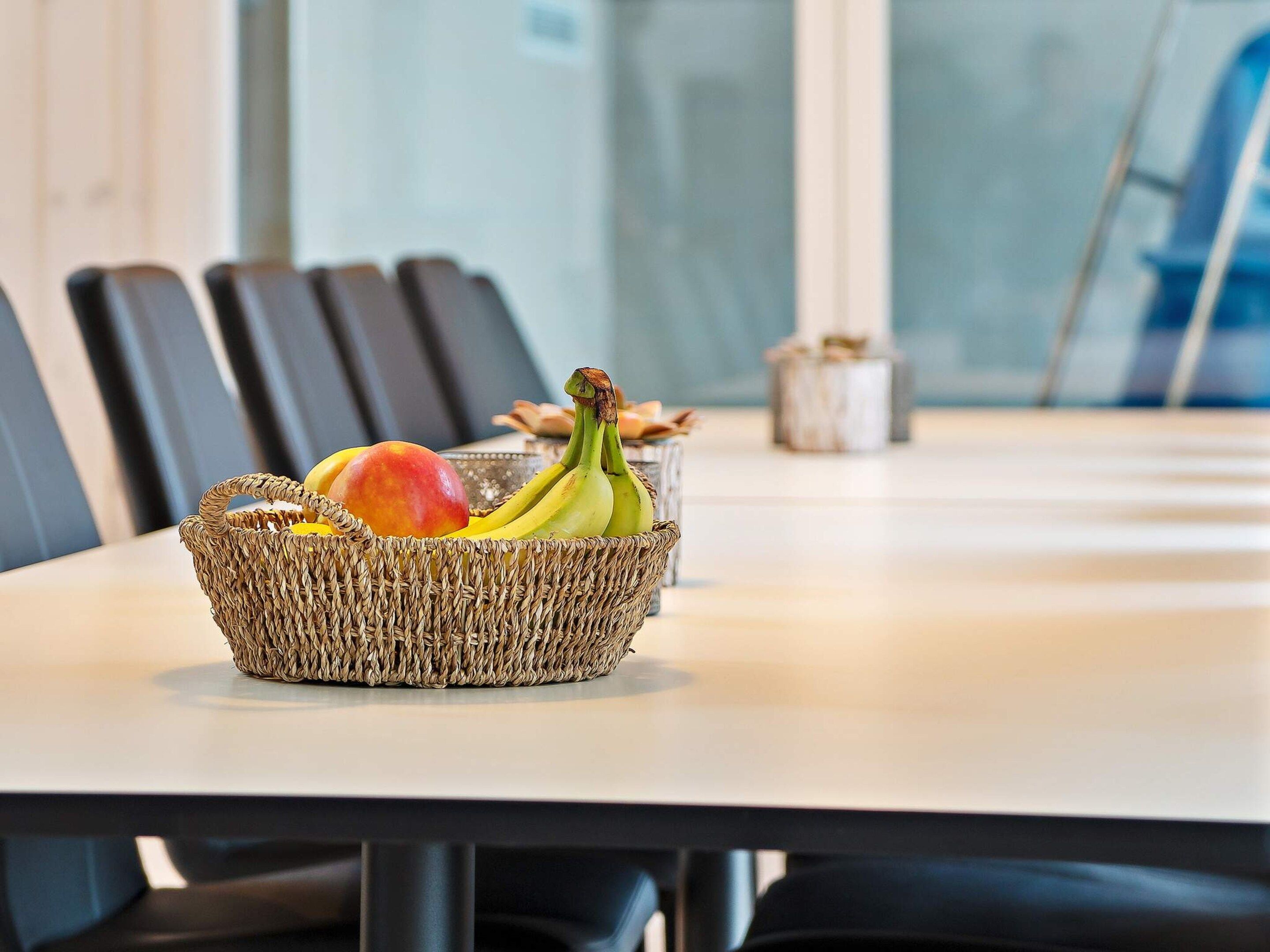 A wicker basket with fruits on a table in a room with chairs and a window.