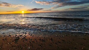 Une plage où le soleil se couche sur l’océan, et où les vagues viennent doucement lécher le rivage.