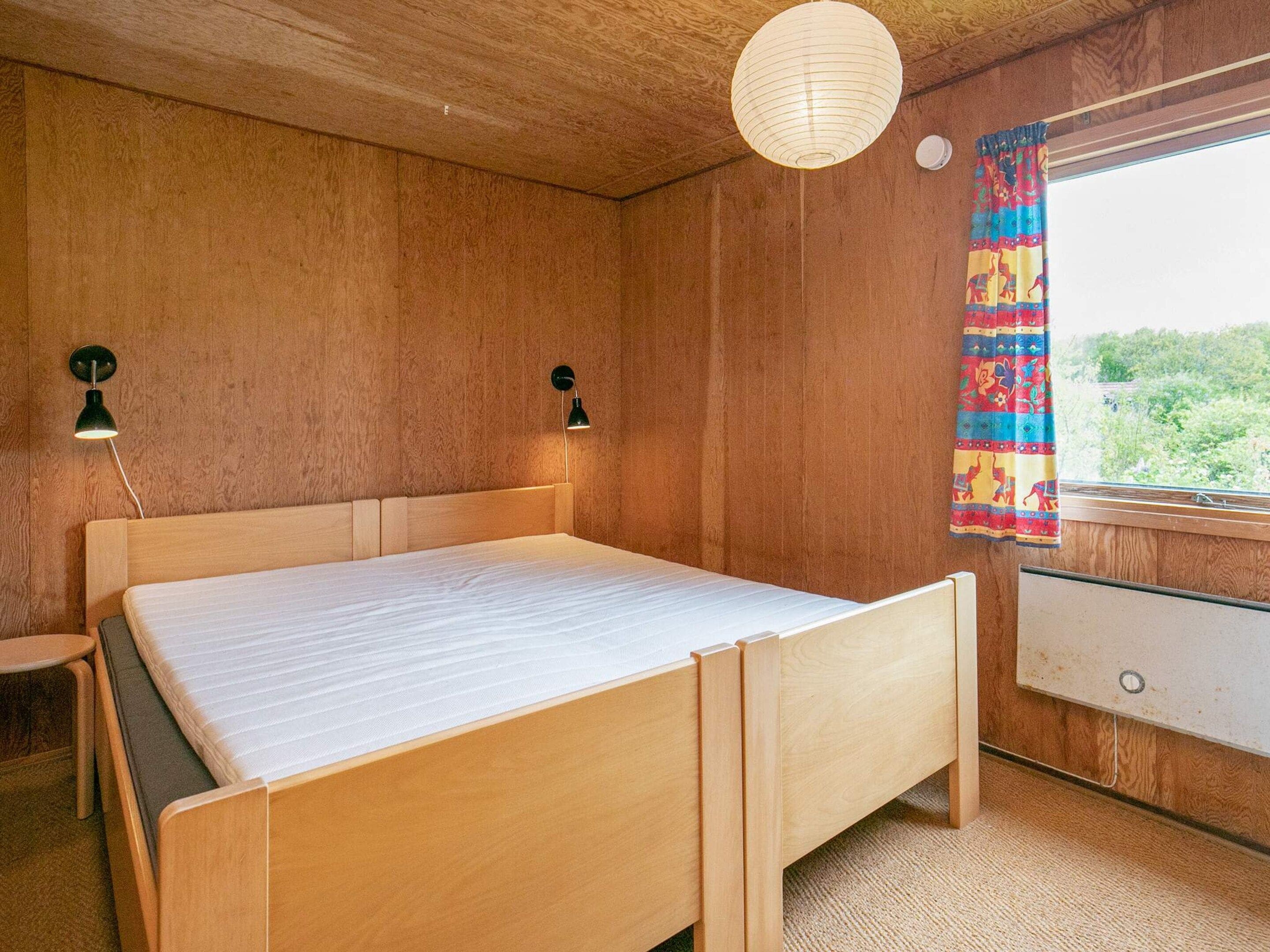 Un dormitorio con cama de madera, dos lámparas fijadas a la pared, un ventanal con cortina y vistas al exterior.