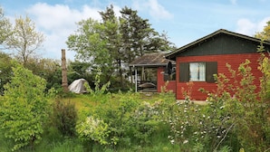 Une cabane rouge avec un porche, entourée d’une végétation luxuriante et d’arbres.