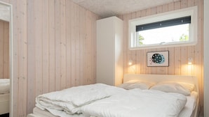 A neatly made bed with white bedding in a room with wooden panel walls and a window with blinds. - Enticing Holiday Home in Ebeltoft near Sea (Ebeltoft)