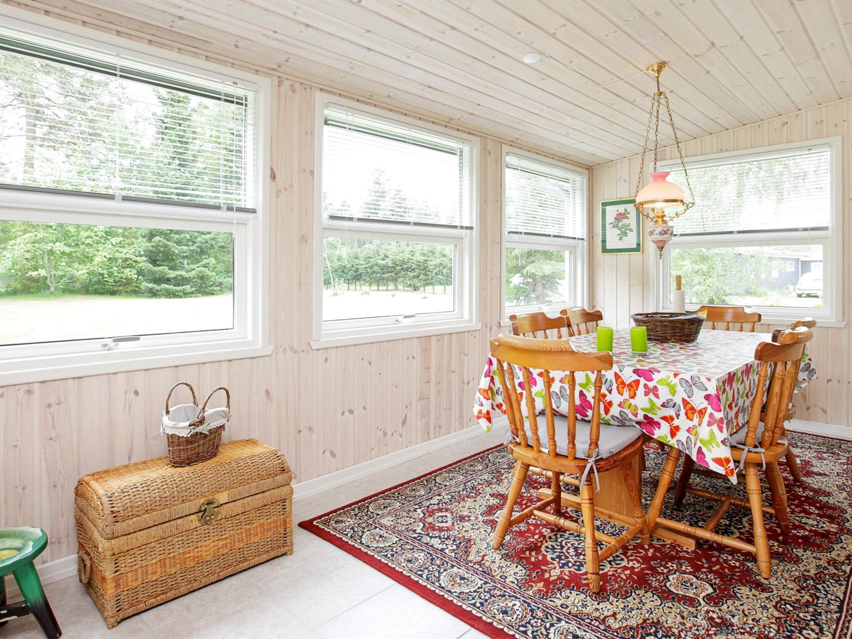 A dining area with a table set for four, surrounded by wooden chairs, a patterned rug, and a wicker chest of drawers.