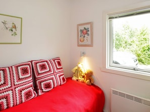 A bed with a red cover, a wall with a framed picture of a bird, and a window with a view of greenery. - Lovely Holiday Home in Jutland near Sea (Hals)