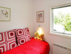 A bedroom with a red bedspread, a wall-mounted lamp, and a window with a view of greenery. - Lovely Holiday Home in Jutland near Sea (Hals)