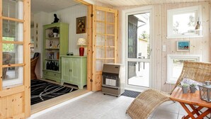 Um quarto aconchegante com teto de madeira, um armário verde, uma mesa com cadeira de fibra natural e uma porta que dá para o exterior.