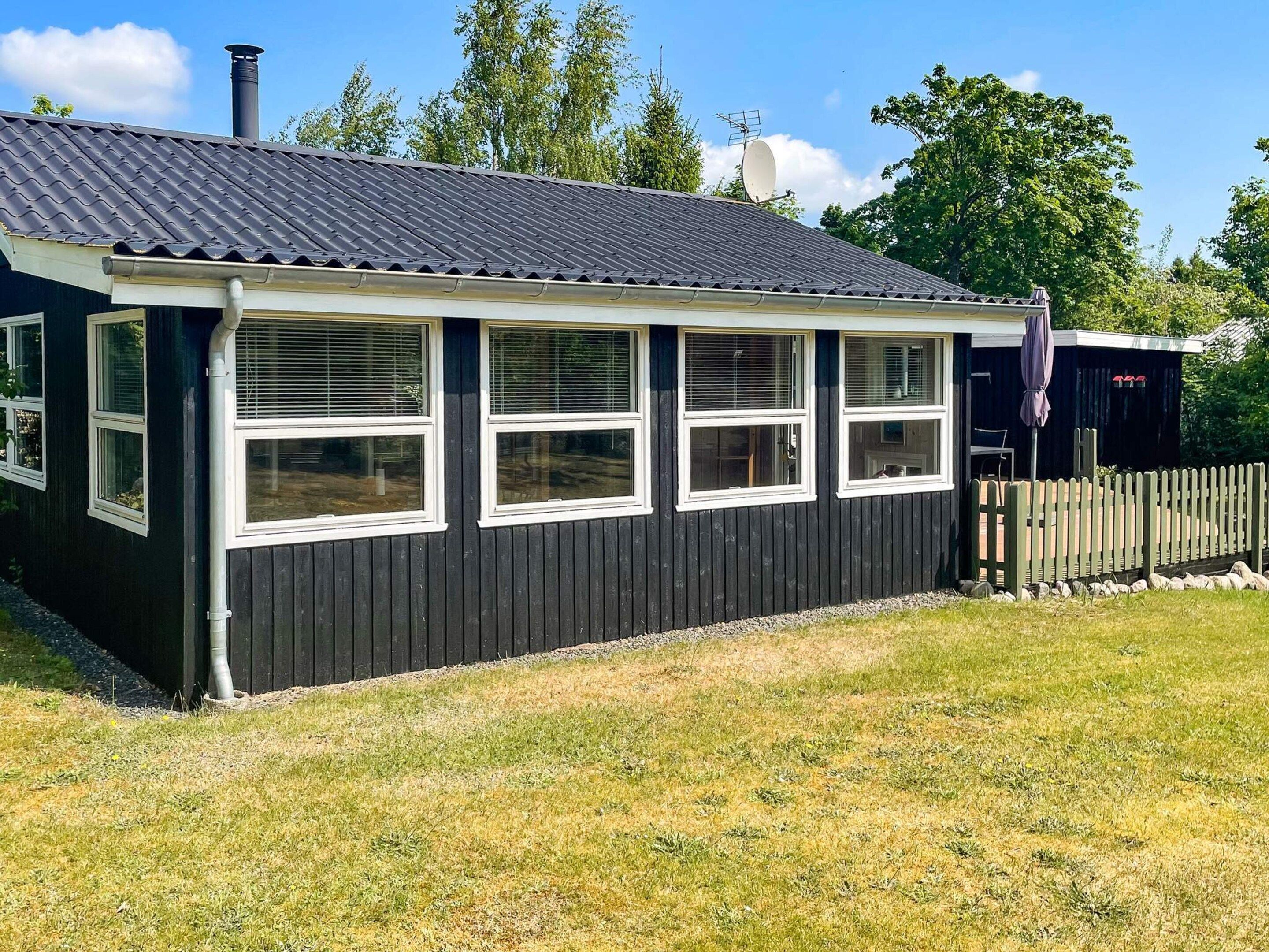 A black building with a tiled roof, multiple windows, and a fenced yard.