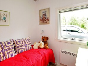 A bedroom with a bed, a teddy bear, a wall-mounted lamp, a framed picture, and a window with a view of a car and greenery outside. - Lovely Holiday Home in Jutland near Sea (Hals)