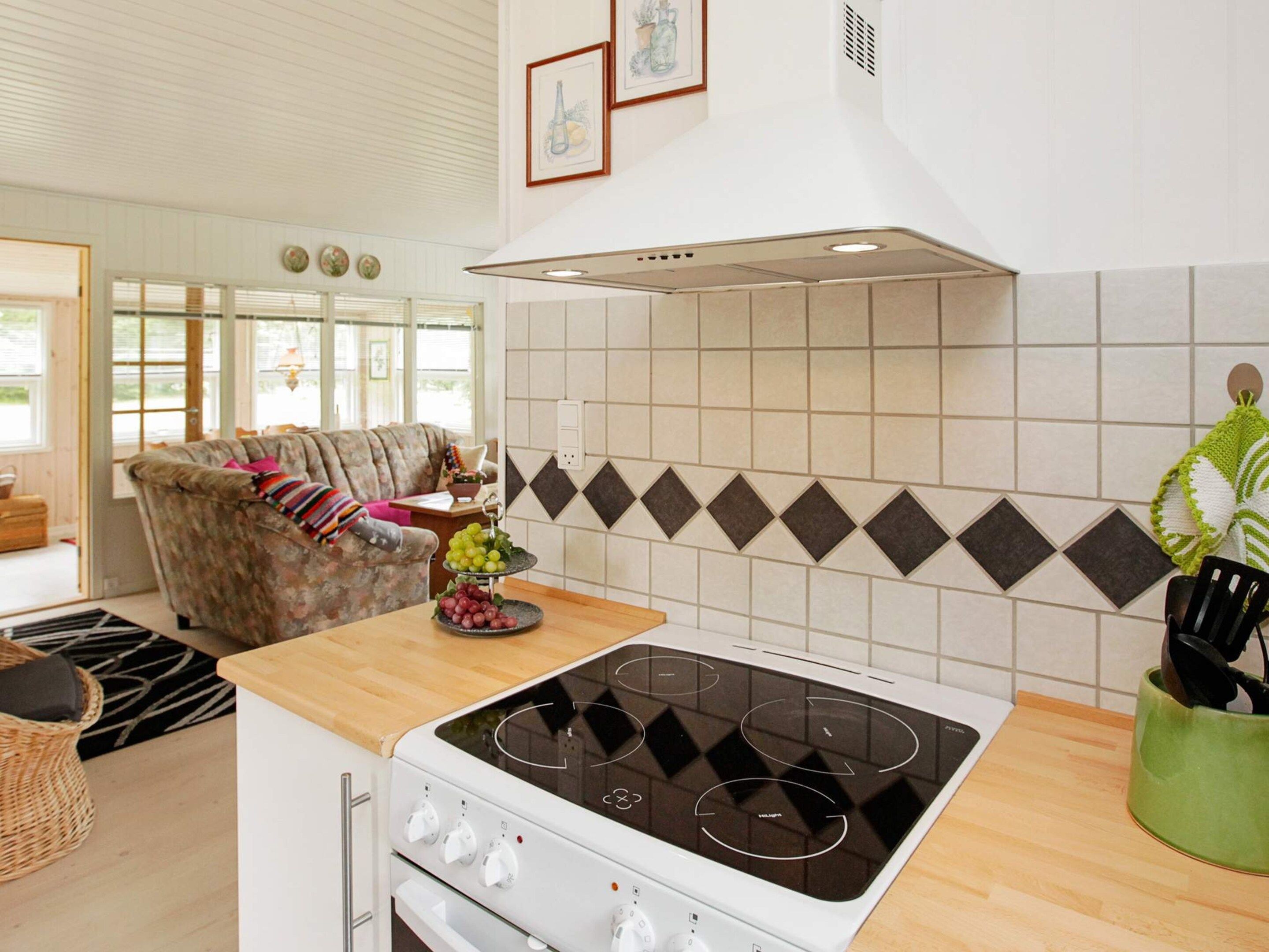 A kitchen with a gas stove, a dining area with a sofa, and a window with blinds.