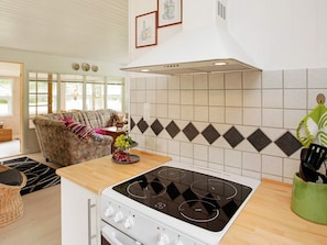 A kitchen with a gas stove, a dining area with a sofa, and a window with blinds. - Lovely Holiday Home in Jutland near Sea (Hals)