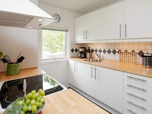 A modern kitchen with white cabinets, a wooden countertop, a sink, a stove, and a window with a view of greenery. - Lovely Holiday Home in Jutland near Sea (Hals)