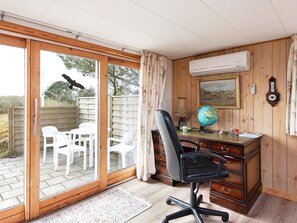 A room with a wooden desk, a black office chair, a globe, a framed painting, and a window with a view of outdoor chairs and greenery. - Enticing Holiday Home in FanÃ¸ near Sea (Fano)