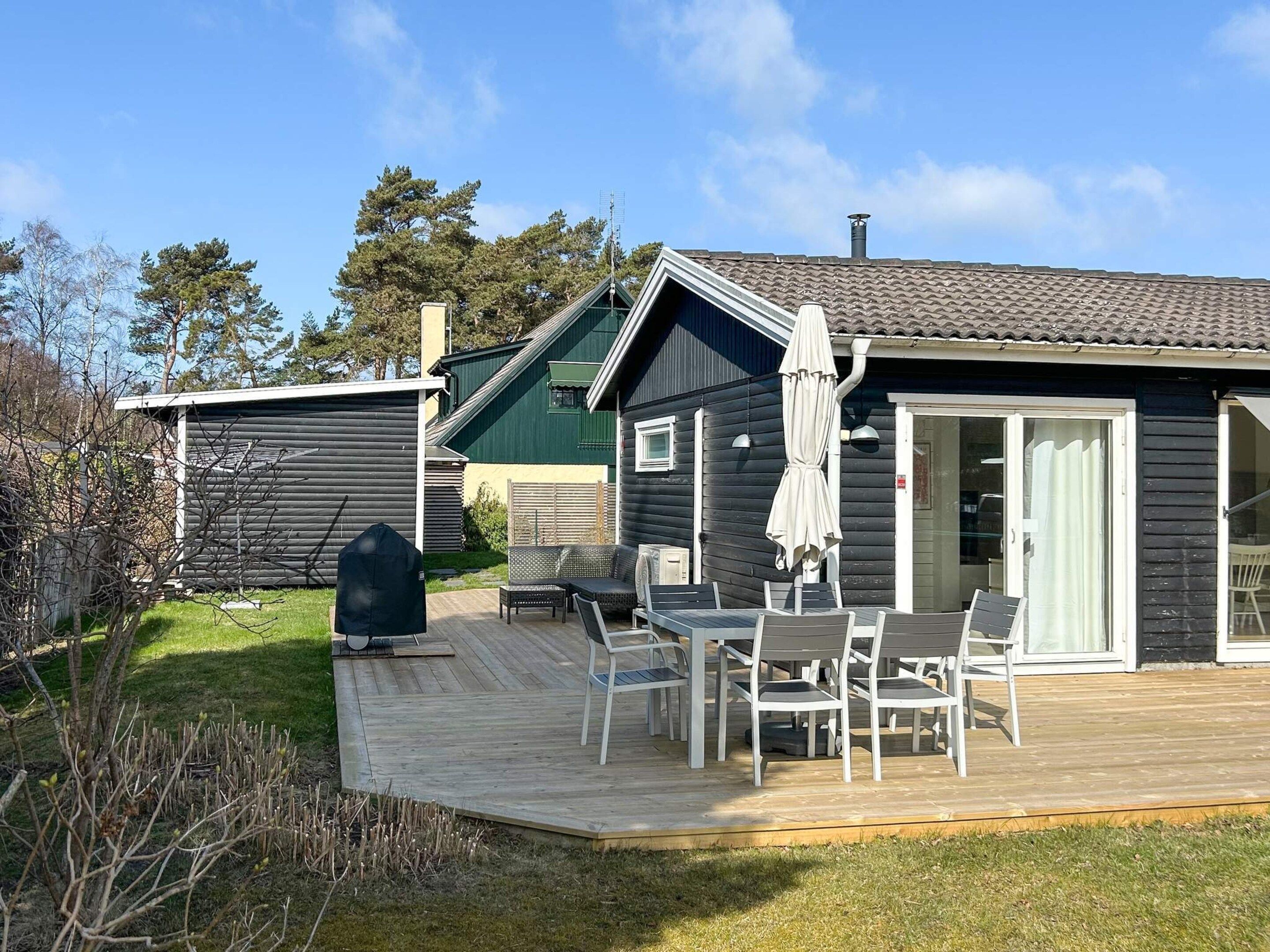 A wooden deck with outdoor furniture, a covered patio area, and a small building with a green roof.
