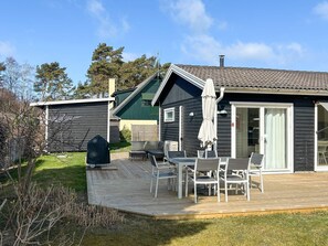 A wooden deck with outdoor furniture, a covered patio area, and a small building with a green roof. - 4 Star Holiday Home in Trelleborg (Trelleborg)