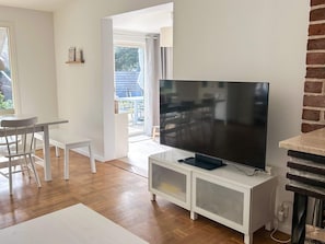 Uma sala de estar moderna com televisão de tela plana, área de jantar com mesa e cadeiras, e cozinha com parede de destaque em tijolos.