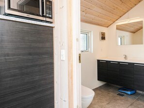 Un baño moderno con techo de madera, inodoro blanco, muebles oscuros y un microondas sobre el lavamanos.