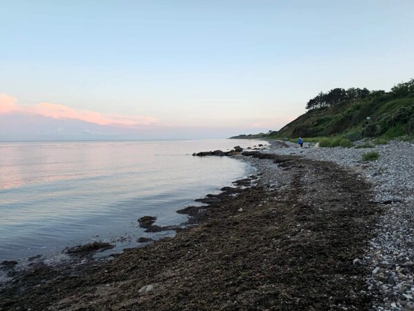 A rocky shoreline with calm water and a person walking along the beach.