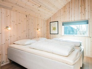 A bedroom with a wooden paneled ceiling and walls, a bed with white bedding, a framed picture on the wall, and a window with blinds.