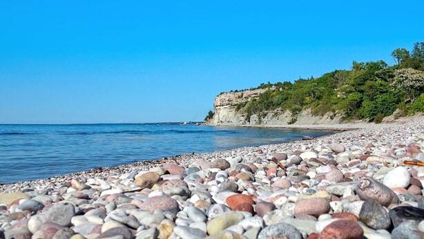 Une plage de galets offrant une vue dégagée sur la mer et une falaise rocheuse couverte de végétation.