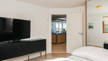 Una habitación de hotel moderna con un televisor de pantalla plana grande, una cama con ropa de cama blanca y vistas al área de la cocina.