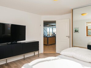 A modern hotel room with a large flat-screen TV, a bed with white bedding, and a view into the kitchen area. - 5 Star Holiday Home in Hojslev (Hojslev)