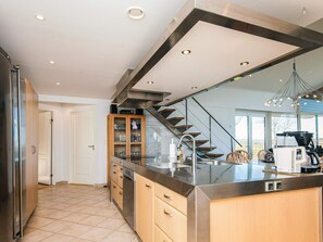 A modern kitchen with a central island, stainless steel appliances, and a wooden cabinet with glass doors. - 5 Star Holiday Home in Hojslev (Hojslev)