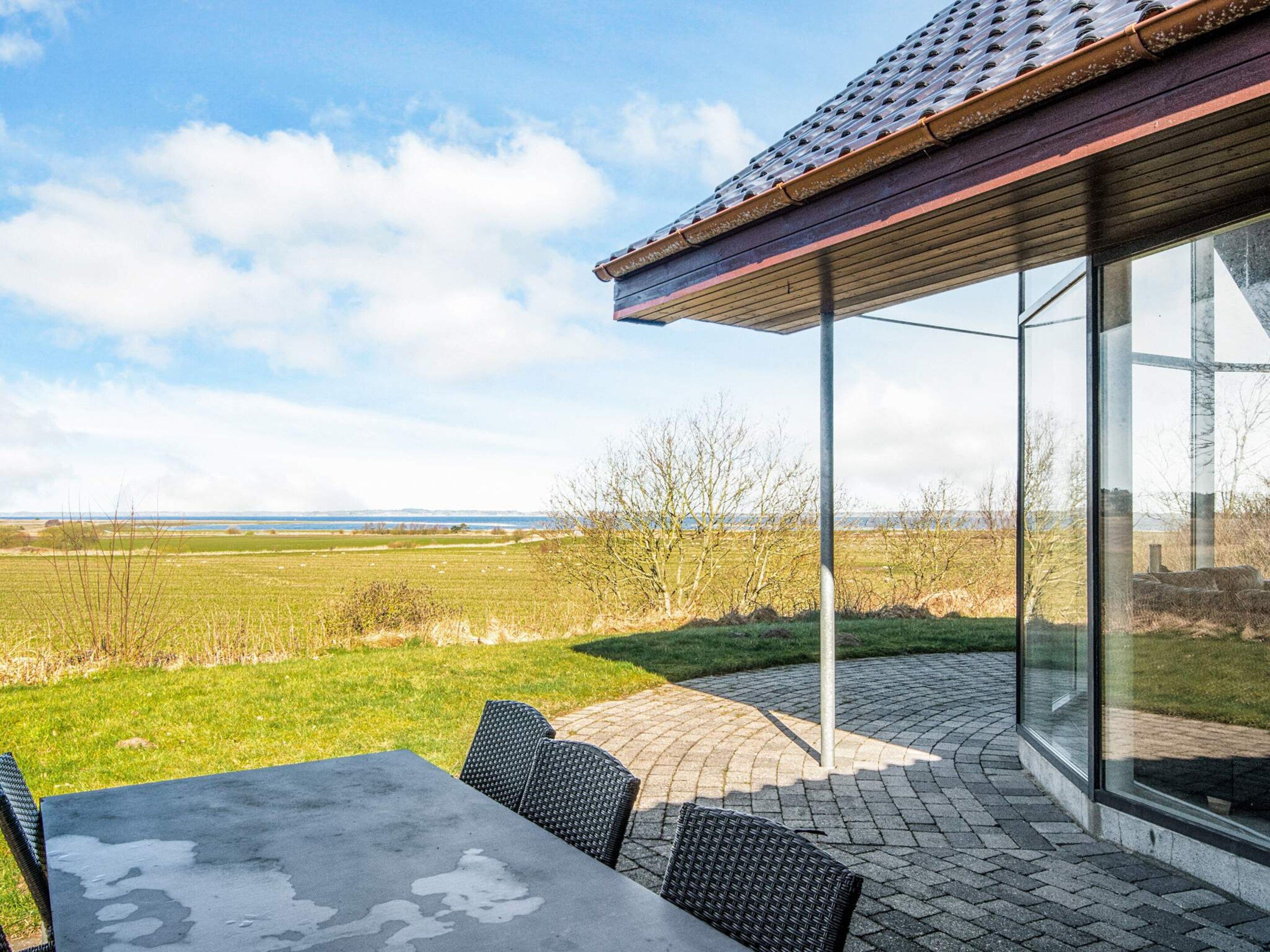 A modern outdoor patio with a table and chairs, overlooking a grassy field and a distant view.