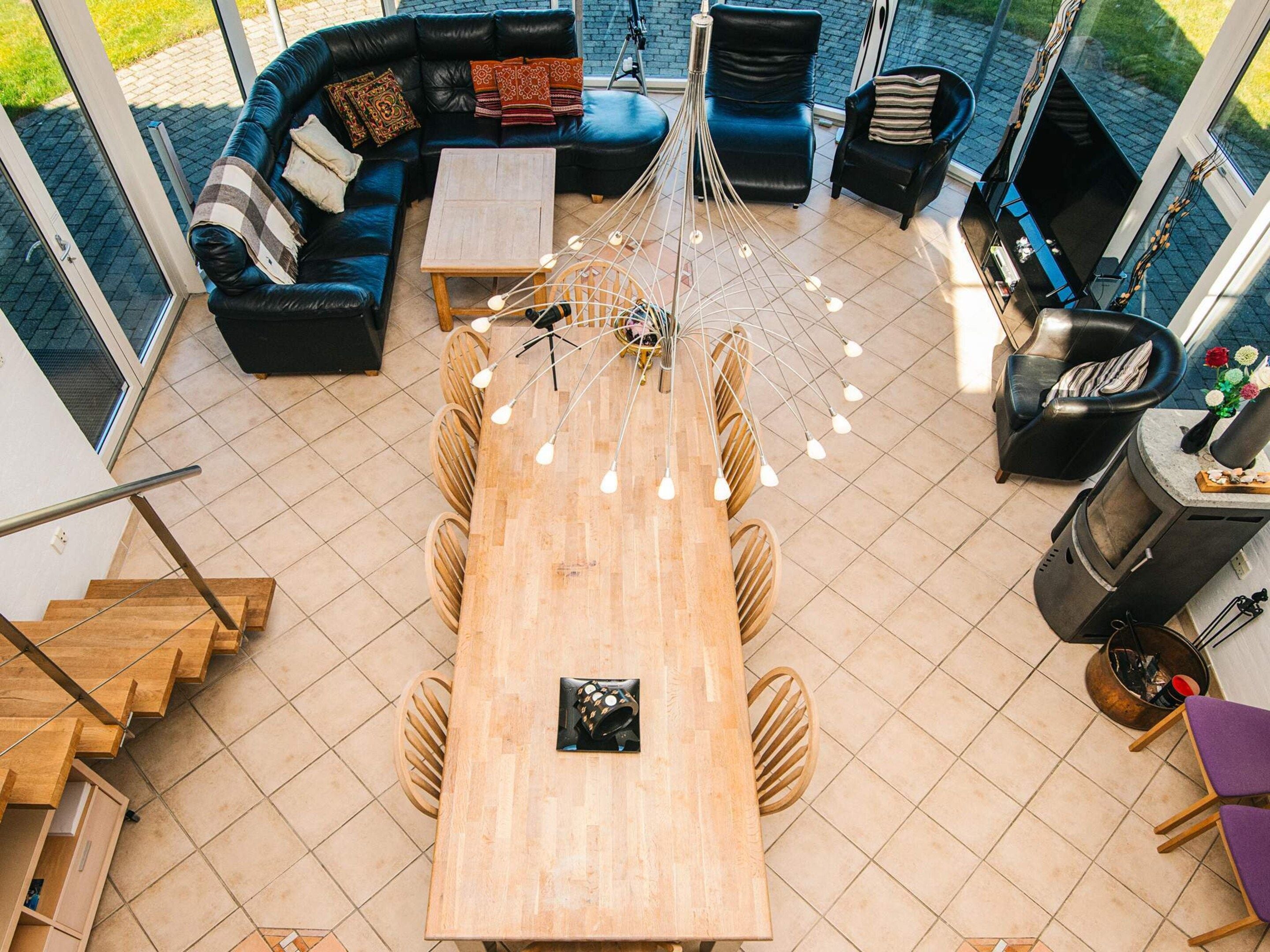 Un salon moderne avec une table à manger en bois, des canapés en cuir noir et un fauteuil noir. On y trouve une cheminée et un escalier menant à un autre niveau.
