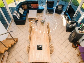 A modern living room with a wooden dining table, black leather sofas, and a black chair. There is a fireplace and a staircase leading to another level. - 5 Star Holiday Home in Hojslev (Hojslev)