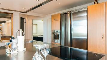 Une cuisine moderne équipée d’un réfrigérateur en acier inoxydable, d’un four et d’un îlot central avec une plaque de cuisson en verre et des verres à vin.
