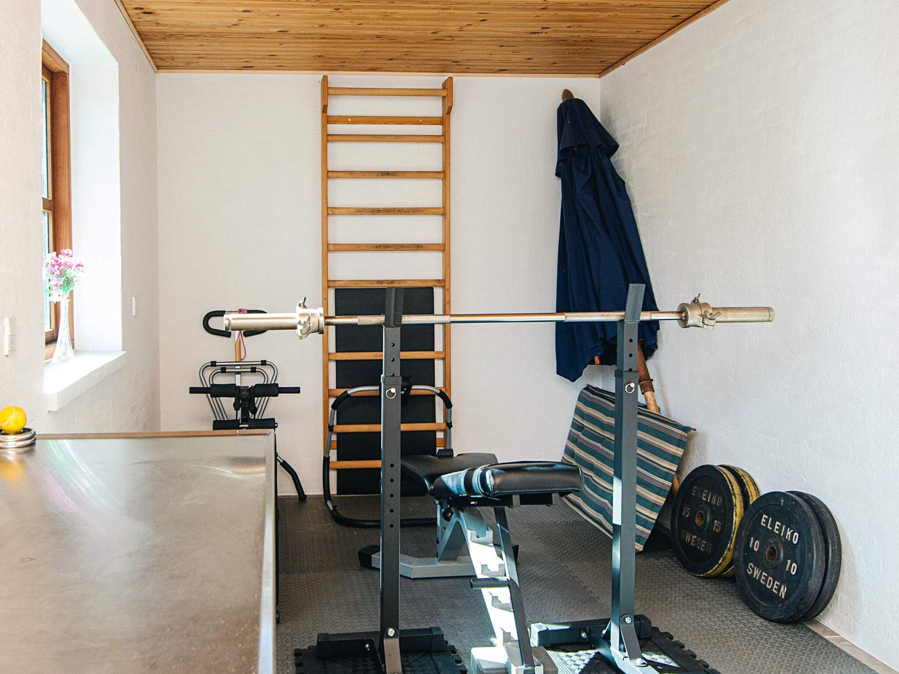 Un gimnasio en casa con una prensa de pesas, una estructura para sentadillas, una barra de dominadas y discos de pesas.