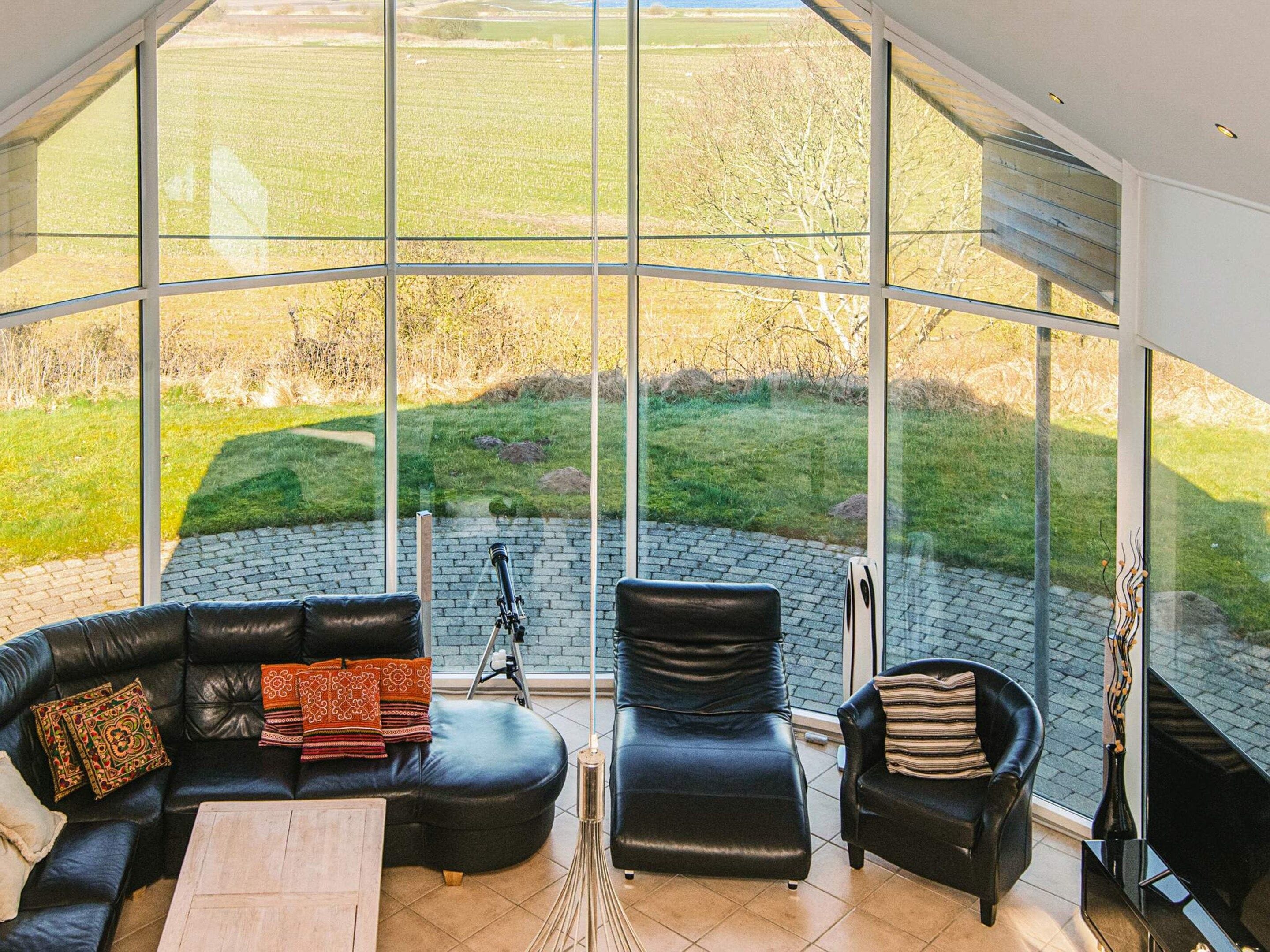 A modern living room with a curved glass wall, leather furniture, and a tripod.