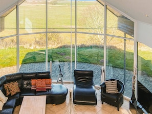 A modern living room with a curved glass wall, leather furniture, and a tripod. - 5 Star Holiday Home in Hojslev (Hojslev)