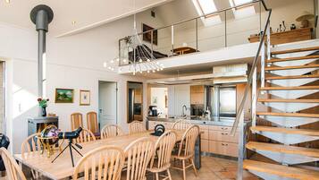 Un comedor amplio con una larga mesa de madera y sillas, una cocina con electrodomésticos modernos y una escalera de caracol que conduce a un nivel superior.