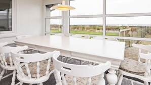 A dining area with a white table and chairs, large windows, and a hanging light fixture. - Holiday Home in Hurup Thy (Hurup Thy)