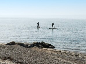 Two individuals paddleboarding on a calm body of water with a rocky shoreline in the foreground. - 6 Person Holiday Home in Hurup Thy (Hurup Thy)