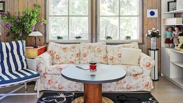A cozy room with a floral sofa, a round wooden table, and a bookshelf with dolls.