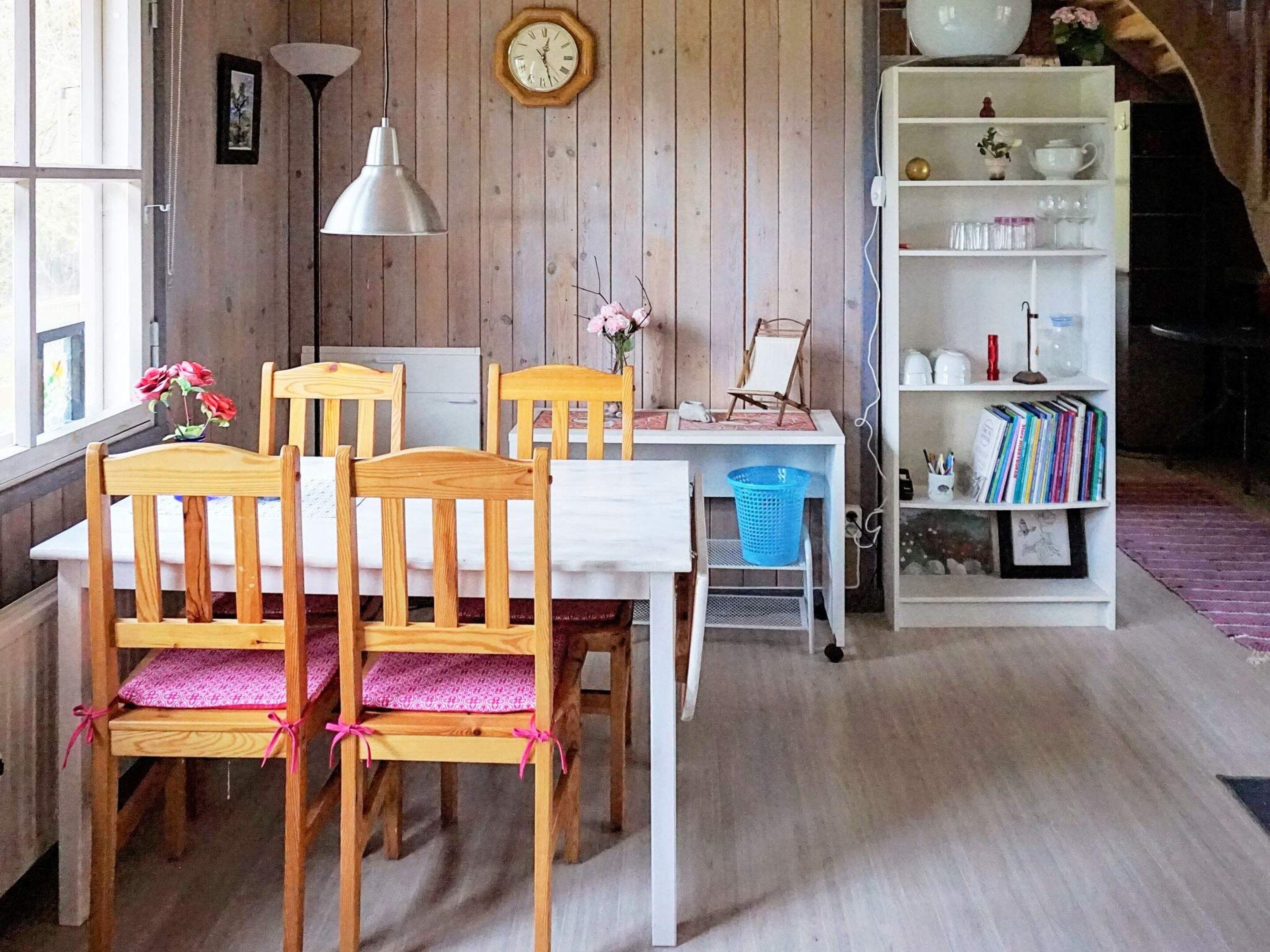 A dining area with wooden chairs, a white table, a clock, and a bookshelf with books and decorative items.