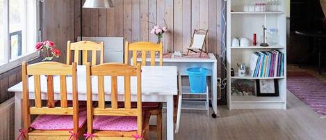 A dining area with wooden chairs, a white table, a clock, and a bookshelf with books and decorative items.