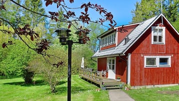A red wooden house with a porch, a pathway leading to the entrance, and a small garden area.