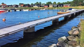 Une jetée s’avançant dans une étendue d’eau calme, où sont amarrés des bateaux, le tout entouré de maisons et de verdure.