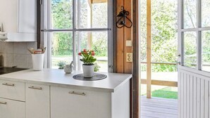 Une cuisine avec des meubles blancs, une fenêtre donnant sur un espace verdoyant et une petite plante en pot posée sur le plan de travail.