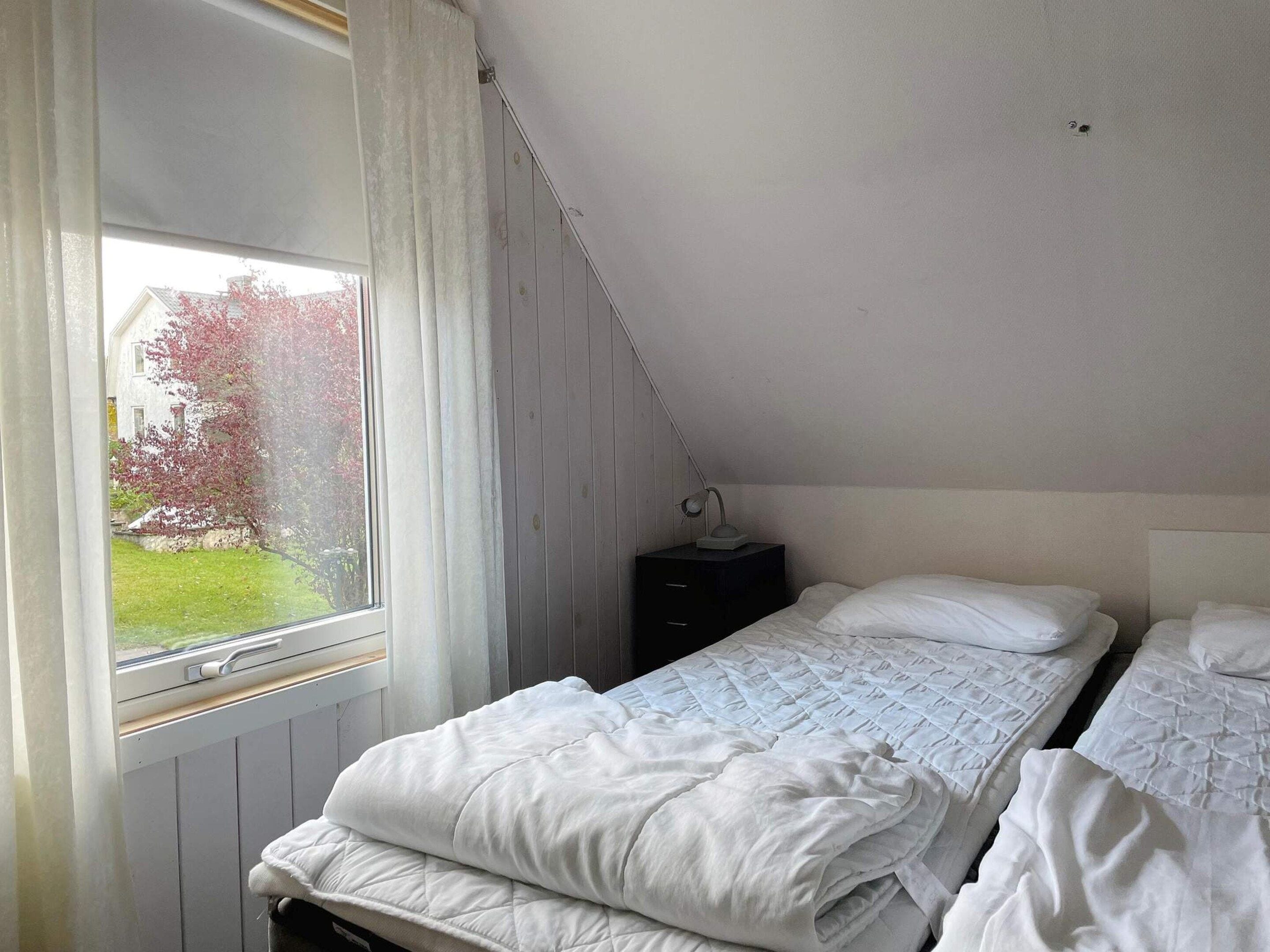 A bedroom with a single bed, a nightstand, and a window with curtains.