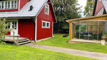 A red house with a sloped roof, a wooden deck, and a glass-enclosed patio area.